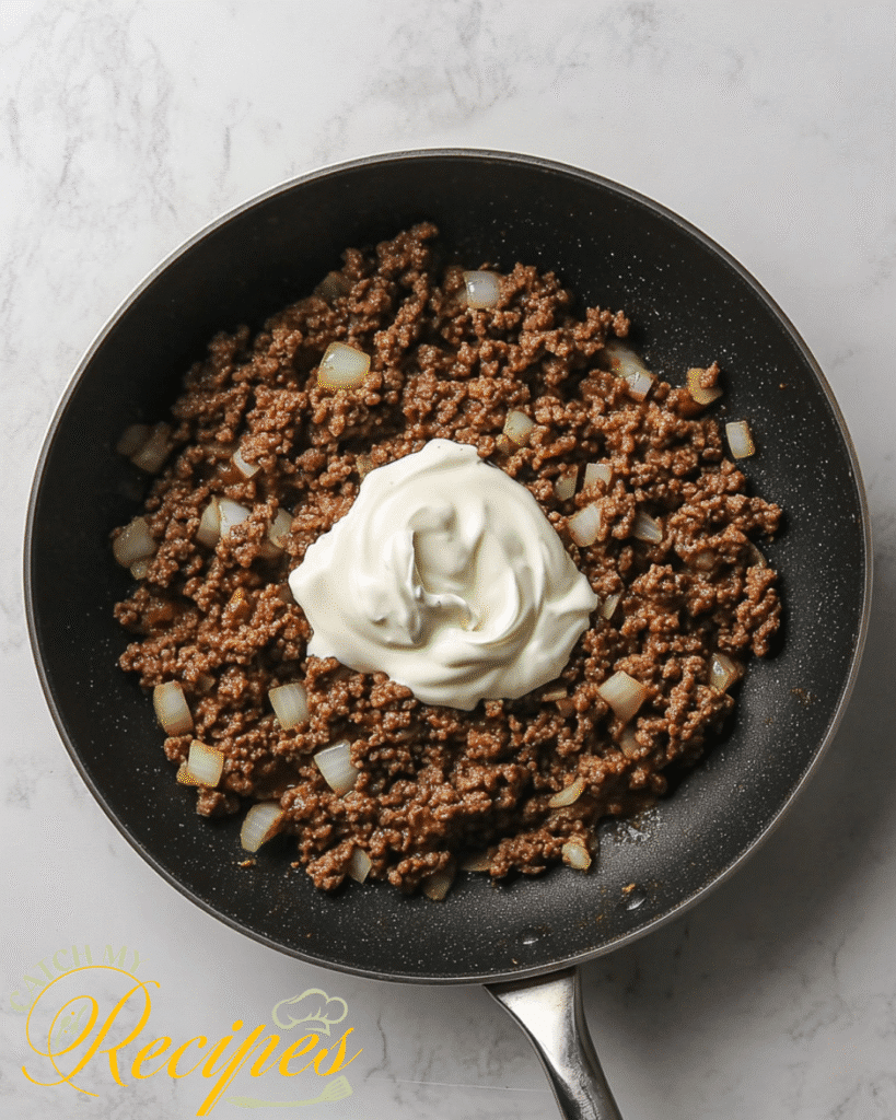 Beef Stroganoff With Potatoes Recipe | 30-Minute Dinner 6 Cooked ground beef and diced onions in a skillet topped with a dollop of sour cream - Step 5