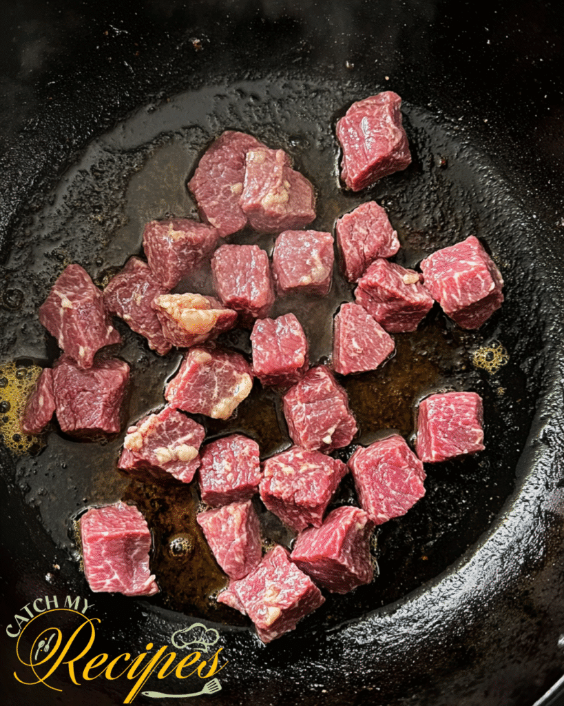 Creamy Dutch Oven Beef Stroganoff 5 Raw beef cubes being seared in a cast iron skillet with oil.
